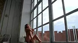 The beautiful babe poses erotically, undressing by the window in this behind-the-scenes video