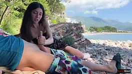 Skinny brunette strokes huge cock to cum on public beach